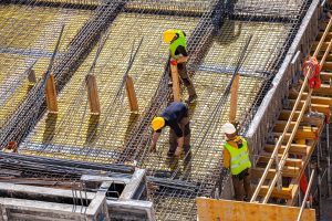 Three construction workers in hard hats use metal bars for reinforced concrete molding