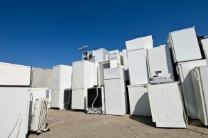 Group of older white refrigerators sitting outside at a scrap yard